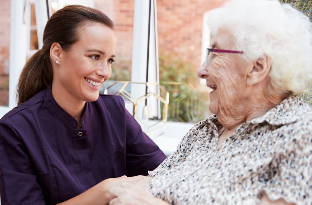 An older adult woman in a memory care facility sitting on a chair smiling and having a conversation with a nurse.