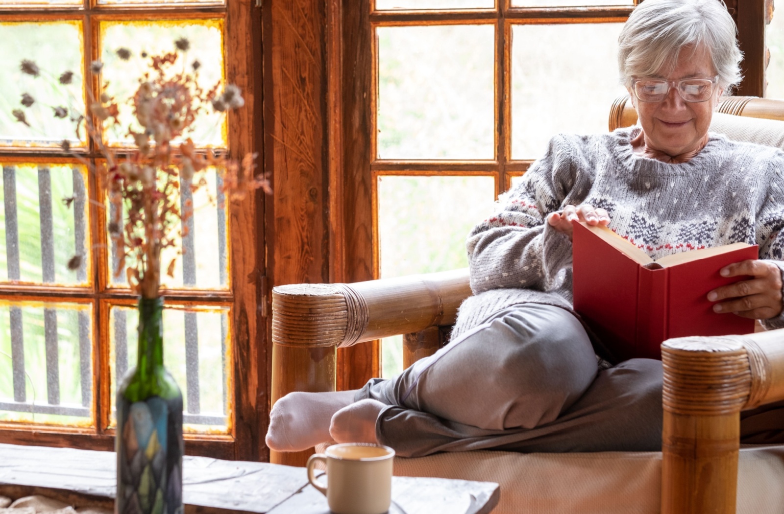 A happy older adult in an armchair reading a book.