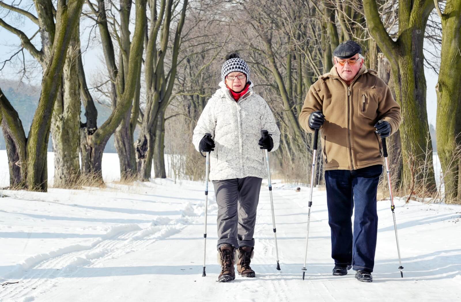 An older couple warmly dressed walking outside in winter with walking poles.