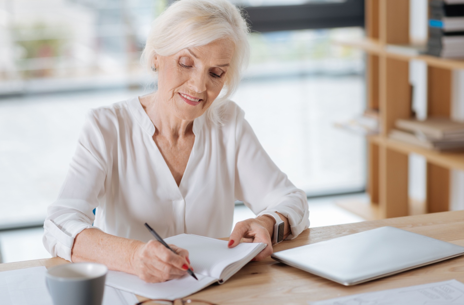 A senior writes in a journal, sitting at a desk in a quiet environment.