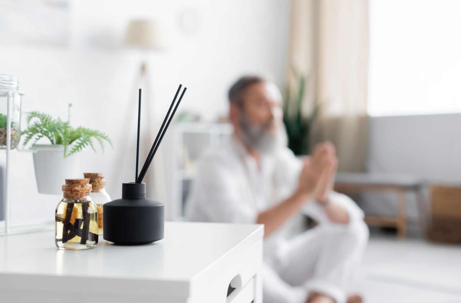 A senior sits on the floor to do some meditation with some diffuser sticks set up on a nearby table for aromatherapy